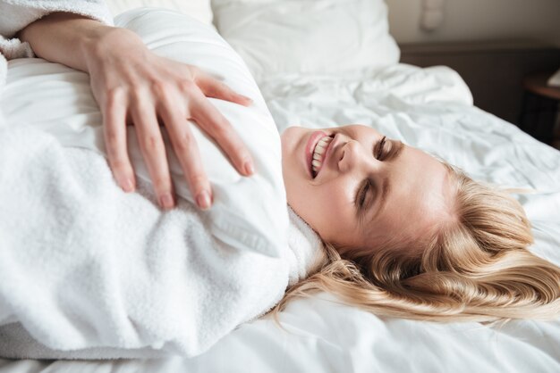 Hübsche blonde Frau im Bademantel, der auf Bett ruht