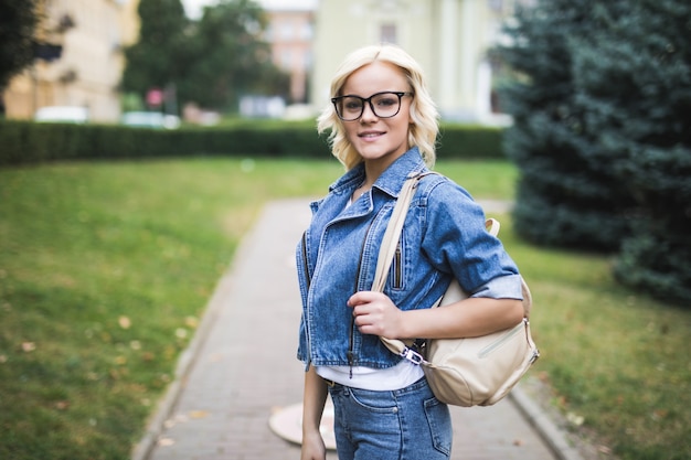 Hübsche blonde Frau im Brillenporträt in der Stadt, die Jeans Suite am Morgen trägt