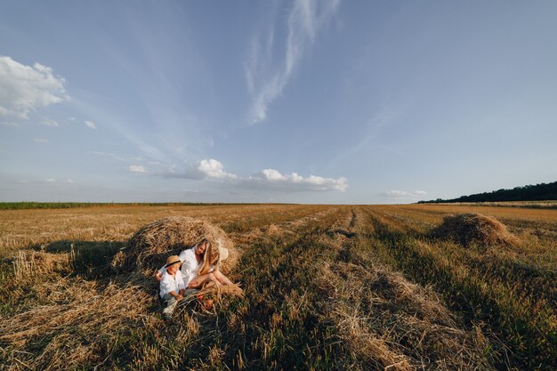 Hübsche blonde langhaarige Frau mit dem kleinen blonden Sohn bei Sonnenuntergang, der sich auf dem Feld entspannt und Früchte aus einem Strohkorb genießt. Sommer, Landwirtschaft, Natur und frische Luft auf dem Land.