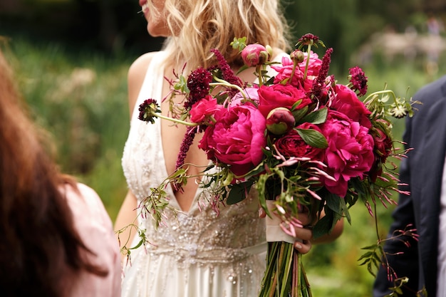 Hübsche Braut hält reichen dunklen rosa Blumenstrauß von Pfingstrosen in ihrem Arm