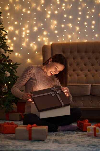 Hübsche brünette Frau öffnet ein entzückendes Geschenk mit Lichtern