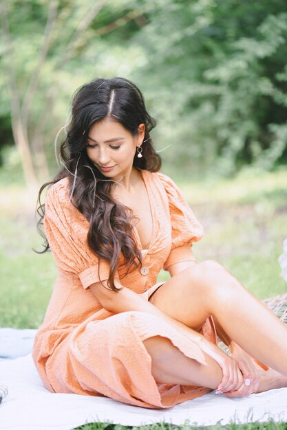 Hübsche Dame im orangefarbenen Kleid, die tagsüber unten in der Natur sitzt und schaut.