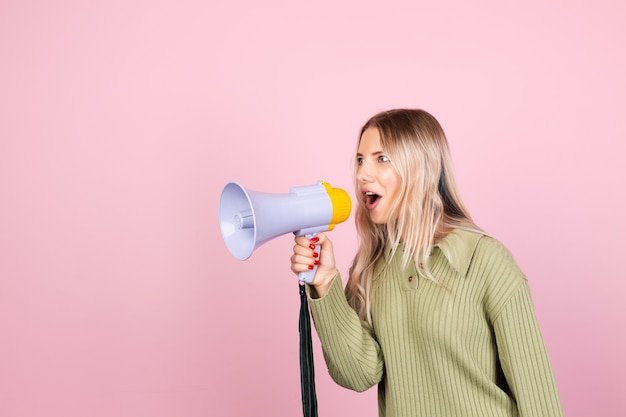 Hübsche europäische frau im lässigen pullover mit megaphon auf rosa wand