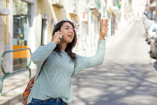 Hübsche Frau, die am Telefon spricht und für Taxi hagelt