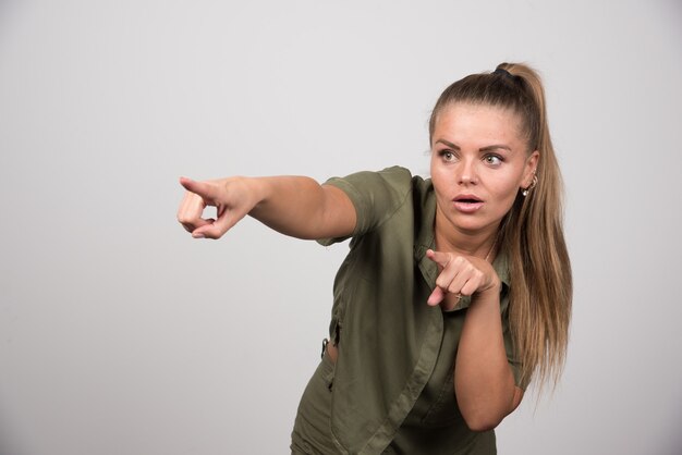 Hübsche Frau, die auf etwas auf grauer Wand zeigt.