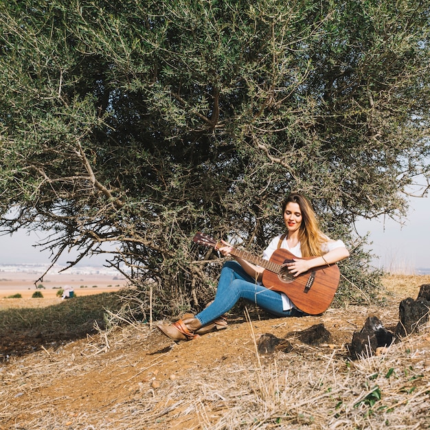 Hübsche Frau, die Gitarre nahe Busch spielt