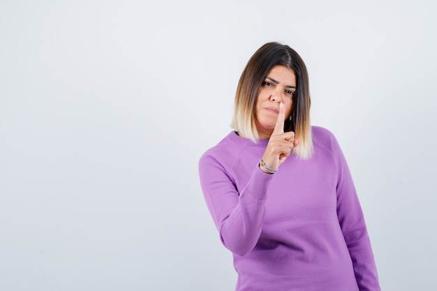 Hübsche Frau, die mit dem Finger im lila Pullover warnt und selbstbewusst aussieht. Vorderansicht.