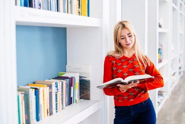 Hübsche Frau, die nahe Bücherschrank liest