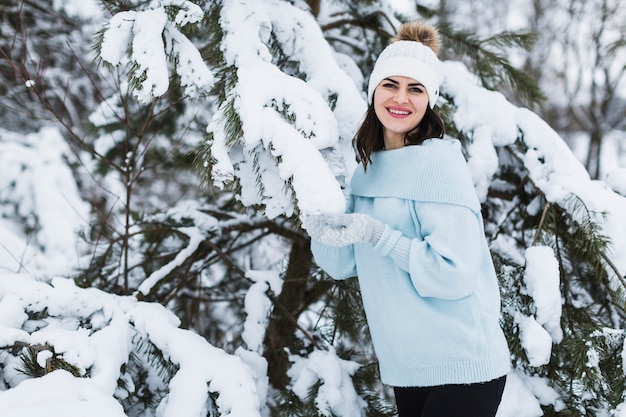 Hübsche Frau, die nahe schneebedeckter Fichte aufwirft