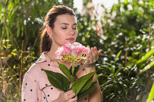 Hübsche Frau, die rosafarbene Blume riecht