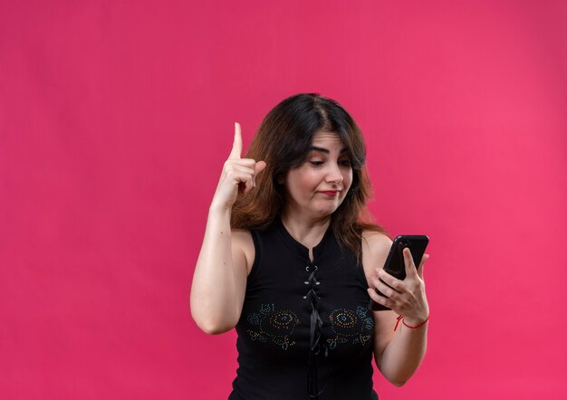 Hübsche Frau, die schwarze Bluse trägt, zeigt oben am Telefon