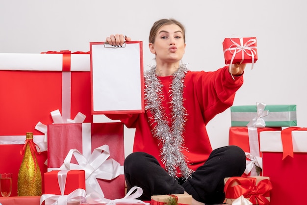 hübsche Frau, die um Weihnachtsgeschenke mit Anmerkung auf Weiß sitzt