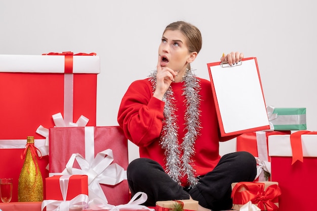 hübsche Frau, die um Weihnachtsgeschenke mit Notiz sitzt, die auf Weiß denkt