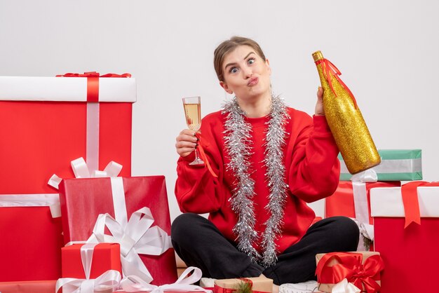 hübsche Frau, die um Weihnachtsgeschenke sitzt, die mit Champagner auf Weiß feiern