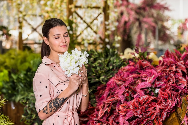 Hübsche Frau, die weiße Blumen im grünen Haus riecht