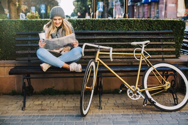 Hübsche Frau, die Zeitung nahe Fahrrad liest