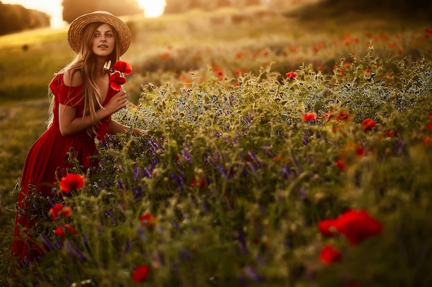 Hübsche Frau geht über ein grünes Feld mit Mohnblumen in den Strahlen der Abendsonne