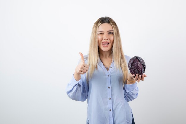 Hübsche Frau im blauen Outfit posiert mit einzelnem Kohl auf weißer Wand.