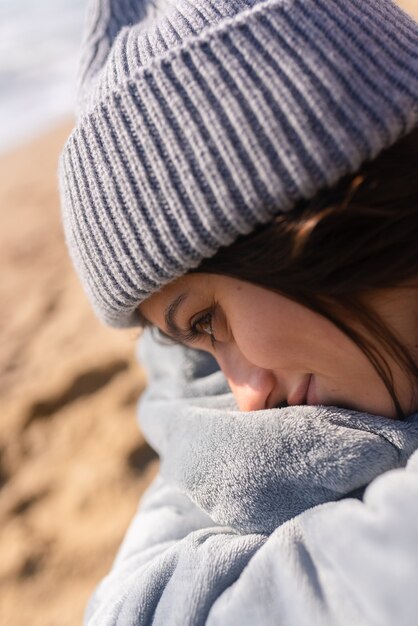 Hübsche Frau in warmer Kleidung, die am kalten Strand sitzt