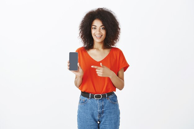 Hübsche Frau mit Afro-Frisur, die mit ihrem Smartphone im Studio aufwirft