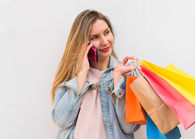 Hübsche Frau mit bunten Einkaufstaschen telefonisch sprechend