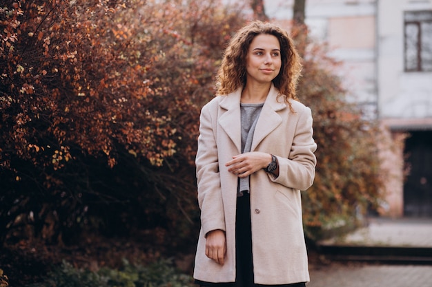 Hübsche Frau mit dem gelockten Haar gehend in einen Herbstmantel