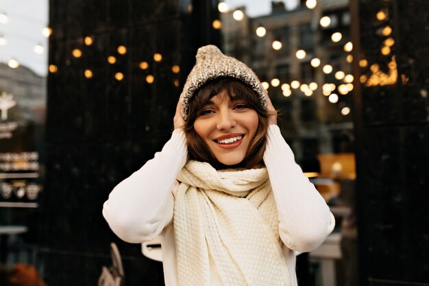 Hübsche Frau mit dunklem Haar, das Spaß außerhalb des modernen niedlichen weiblichen Getränks hat, das Weihnachten auf Stadthintergrund vorbereitet Hochqualitätsfoto