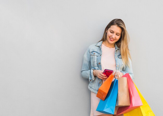 Hübsche Frau mit Einkaufstüten mit Smartphone