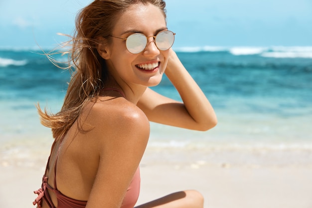 Hübsche Frau mit Sonnenbrille und Badeanzug am Strand