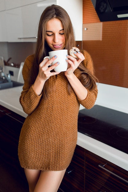 Hübsche Frau mit weißer Tasse Tee in der modernen Küche auf sonniger Herbstmorgenzeit.