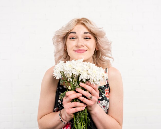 Hübsche Frau, welche die weißen Blumen betrachten Kamera hält