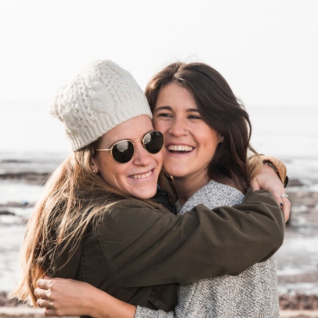 Hübsche Frauen, die auf Seehintergrund umarmen