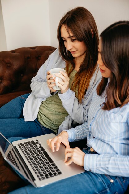 Hübsche Frauen, die Laptop auf Couch durchstöbern