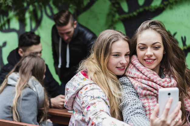 Hübsche Frauen, die selfie an der grünen Wand nehmen