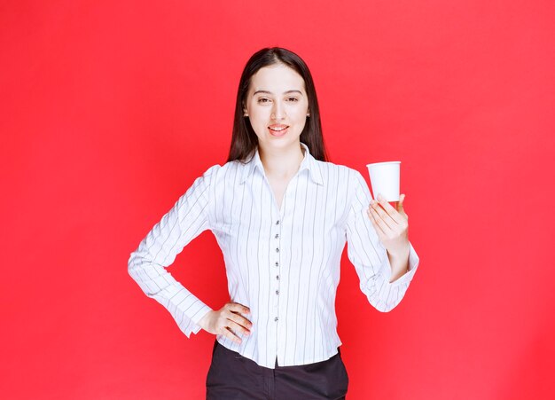 Hübsche Geschäftsfrau, die mit Plastiktasse Tee auf rotem Hintergrund aufwirft.
