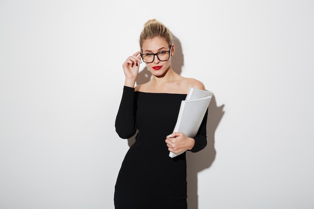 Hübsche Geschäftsfrau im Kleid und in Brillen, die Dokumente verwahren