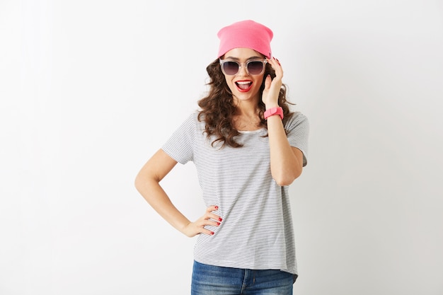 Hübsche hübsche Hipster-Frau im rosa Hut, Sonnenbrille, lächelnd, isoliert, weiße Zähne, rote Lippen, lockiges Haar, T-Shirt tragend