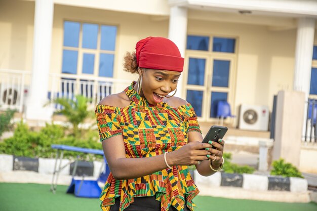 Hübsche junge afrikanische Dame, die ihr Telefon hält und sich aufgeregt fühlt