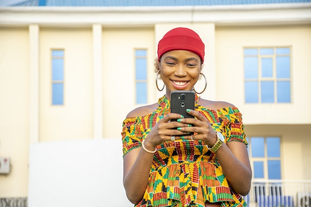 Hübsche junge afrikanische Frau, die lächelt und ihr Handy im Freien benutzt
