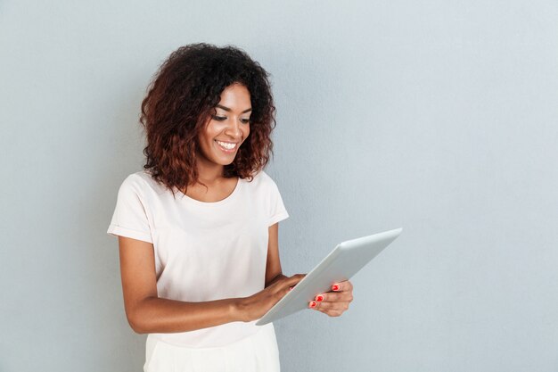 Hübsche junge afroamerikanische Frau, die steht und Tablette verwendet