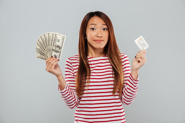 Hübsche junge asiatische Dame, die Geld und Kreditkarte hält.