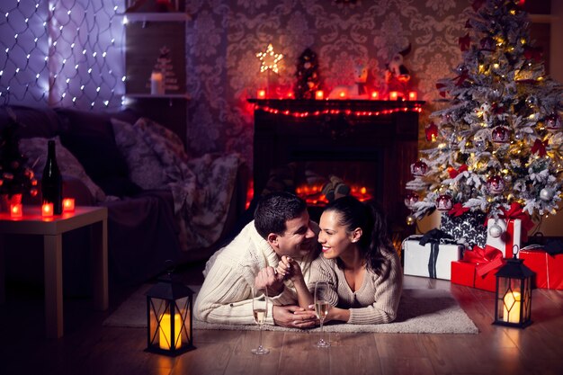 Hübsche junge Frau, die einen süßen Moment mit ihrem Freund im Wohnzimmer nahe Weihnachtsbaum hat. Weihnachtsfest.