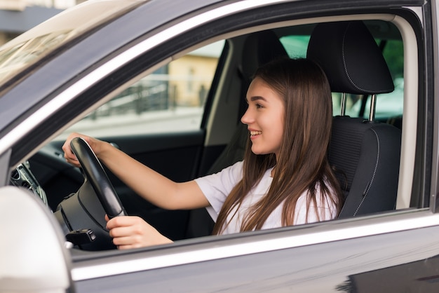 Hübsche junge Frau, die ihr neues Auto auf der Straße fährt