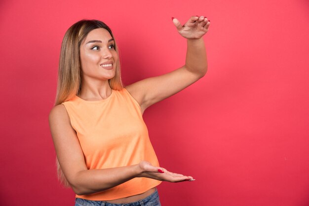 Hübsche junge Frau, die leeren Raum auf Handfläche hält und ihre Seite schaut.