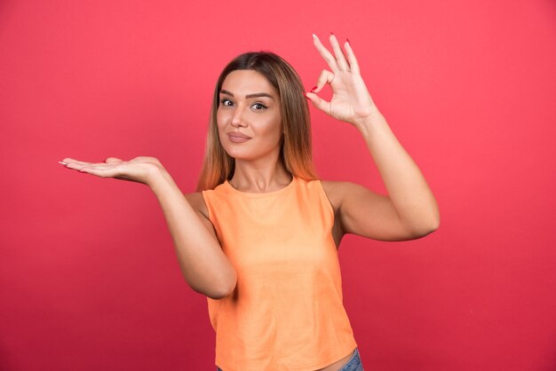 Hübsche junge Frau, die ok Zeichen auf roter Wand macht.