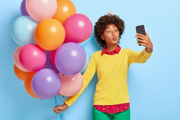 Hübsche junge Frau hält bunte Luftballons, während sie in einem gelben Pullover posiert