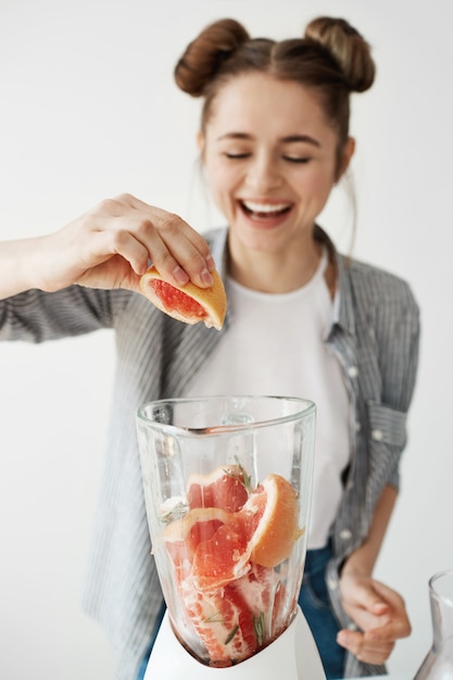 Kostenloses Foto hübsche junge frau lächelnd, die entgiftung erfrischenden grapefruitsmoothie über weißer wand mischt. gesundes lebensmittelkonzept.