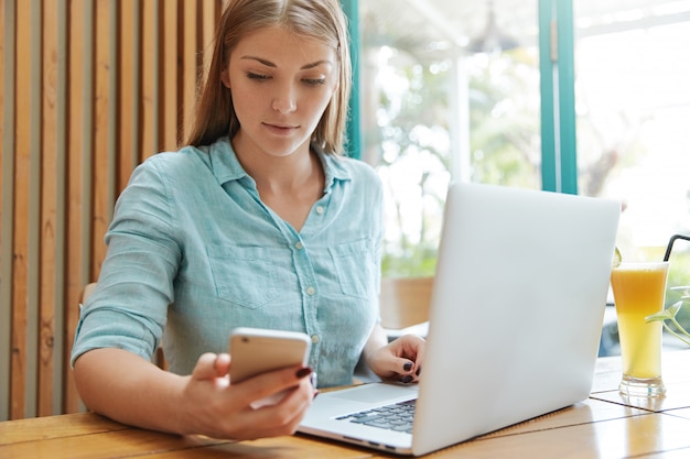 Hübsche junge Frau mit langen Haaren, die im Café mit Laptop sitzen