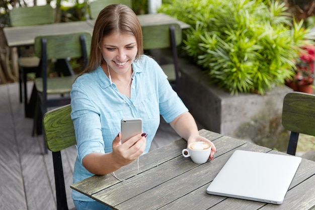 Hübsche junge Frau mit langen Haaren, die im Café mit Telefon sitzt