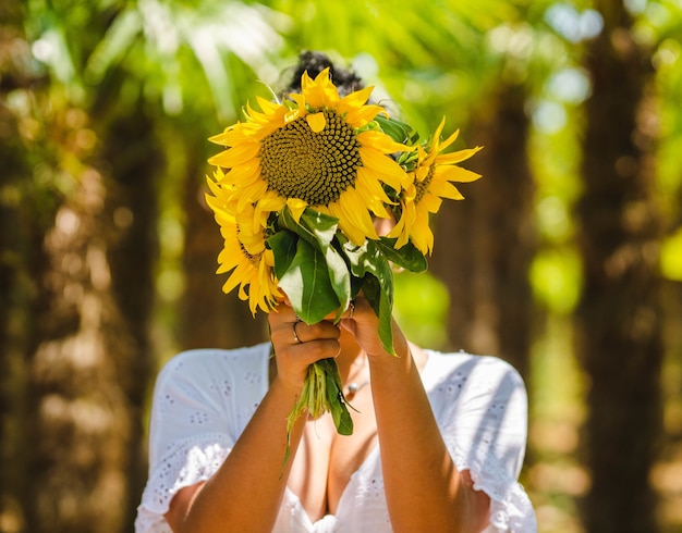 Hübsche junge Frau versteckt ihr Gesicht hinter einem Strauß Sonnenblumen